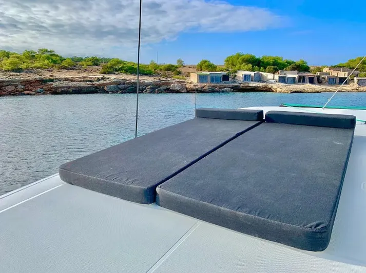  Yacht Photos Pics 2024 Lagoon 42 catamaran with sunbathing cushions, anchored near a scenic shoreline.