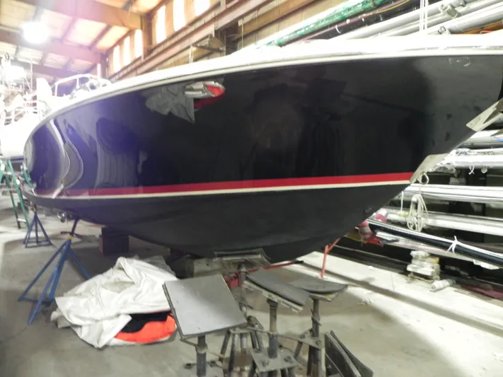 Yours To Name Yacht Photos Pics 2015 Chris-Craft 28 Heritage Corsair boat in storage, featuring sleek black hull with red stripe.
