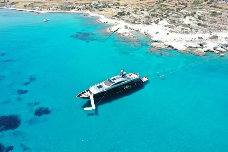 Lucky Me Yacht Photos Pics Aerial view of a 2010 Baglietto 41 yacht anchored in clear turquoise waters near a rocky coastline.