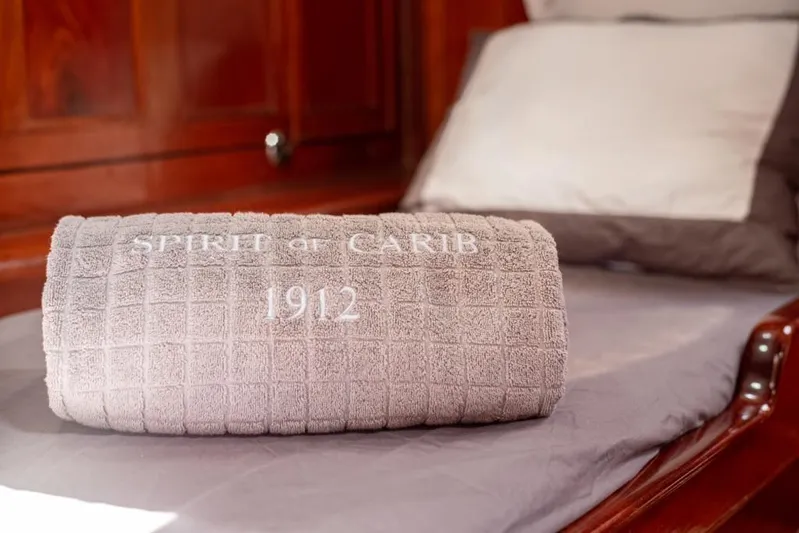  Yacht Photos Pics Rolled towel on yacht bed, embroidered with "Spirit of Carib 1912," wooden interior.