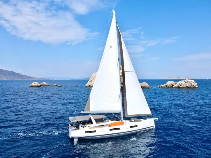 Euphoria Yacht Photos Pics 2021 Jeanneau 60 sailboat navigating clear blue waters near rocky islands.