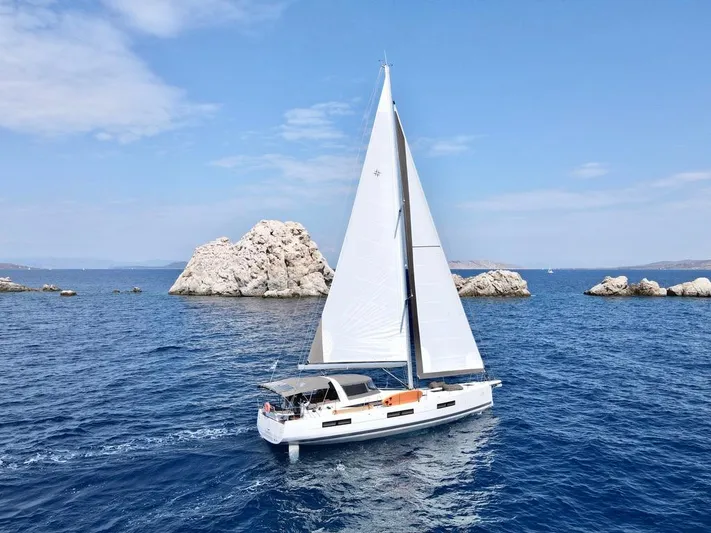 Euphoria Yacht Photos Pics 2021 Jeanneau 60 sailboat cruising near rocky islands on a clear blue sea.