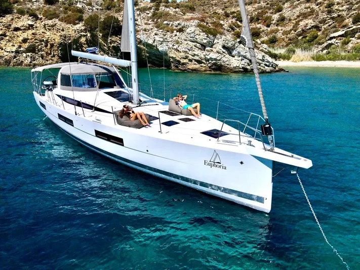 Euphoria Yacht Photos Pics 2021 Jeanneau 60 yacht anchored in clear blue water near rocky coastline.