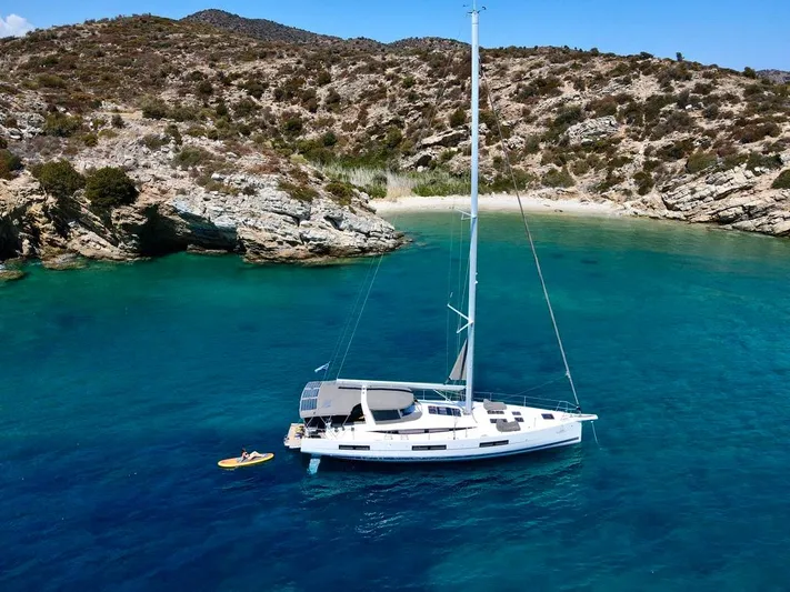 Euphoria Yacht Photos Pics 2021 Jeanneau 60 yacht anchored in a serene, turquoise bay with rocky hills.