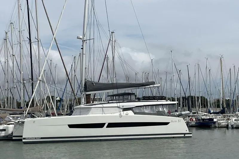Maeva Yacht Photos Pics 2023 Fountaine Pajot Catamaran Aura 51 docked in a marina with sailboats.