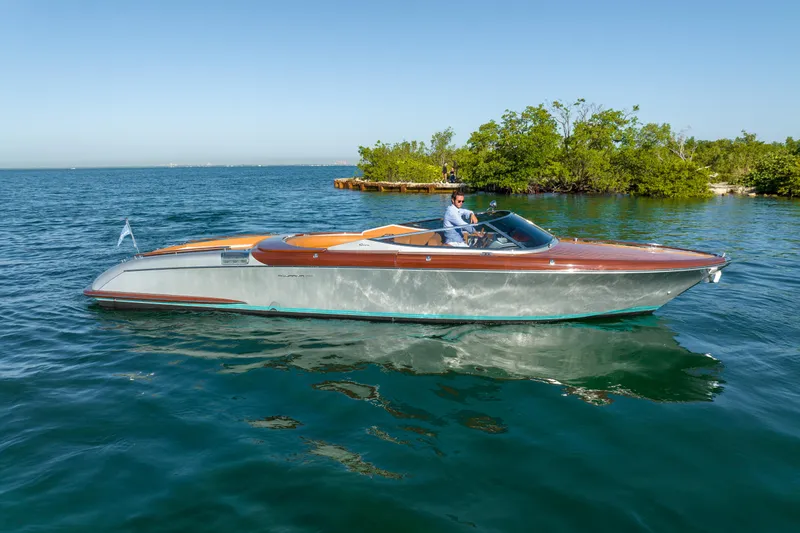 Mia Mia Yacht Photos Pics 2020 Riva Aquariva luxury speedboat cruising on clear blue water near a lush green island.