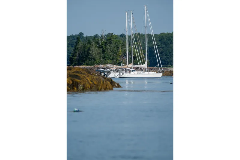 Boojum Yacht Photos Pics Sailboat Outbound 46, 2024 model, anchored near rocky shoreline with forested background.