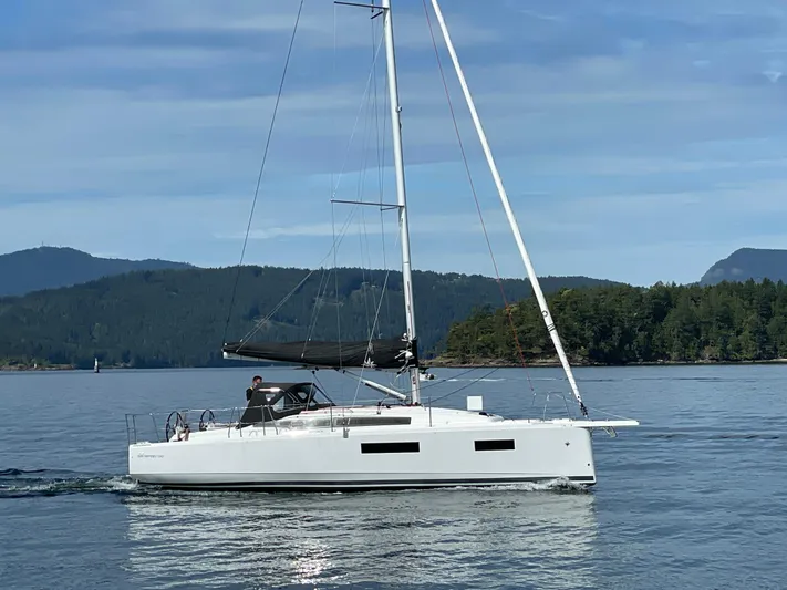  Yacht Photos Pics 2024 Jeanneau Sun Odyssey 350 sailing on calm waters with scenic forested hills.