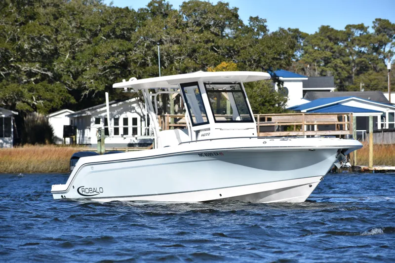  Yacht Photos Pics 2022 Robalo R272 Center Console boat on water, surrounded by trees and houses.
