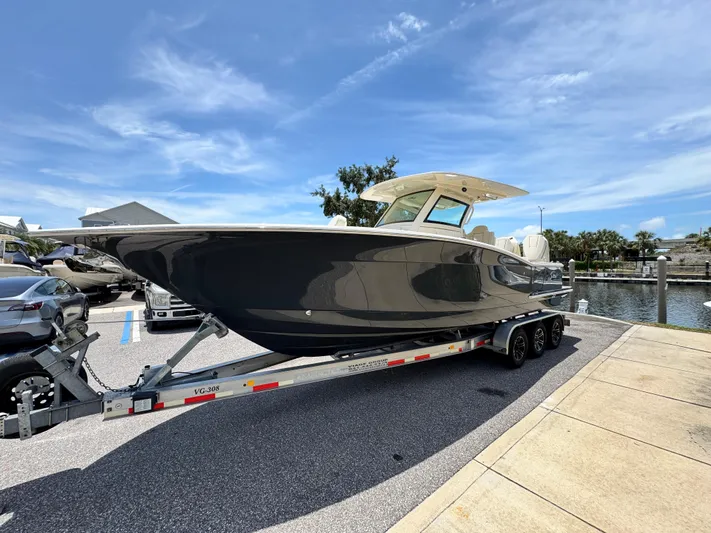  Yacht Photos Pics 2025 Scout 305 LXF boat on trailer, parked near waterfront under clear blue sky.