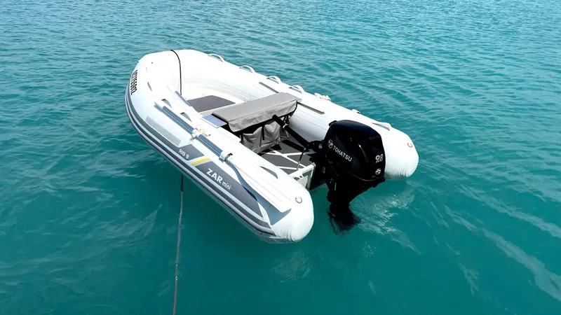 Libertad Yacht Photos Pics A white inflatable boat with an outboard motor floating on clear blue water.