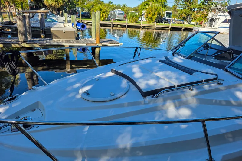  Yacht Photos Pics 2022 Monterey 295 Sport Yacht docked at a marina, surrounded by calm water and lush greenery.