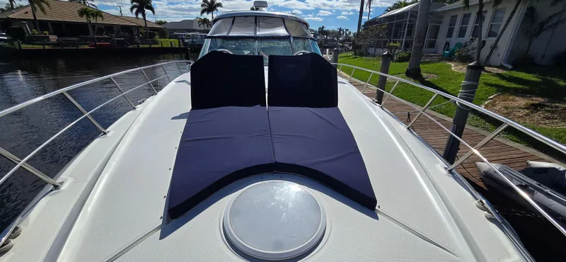 Off Line Yacht Photos Pics 2006 Cruisers Yachts 52 Express with sun pads on deck, docked by waterfront homes.