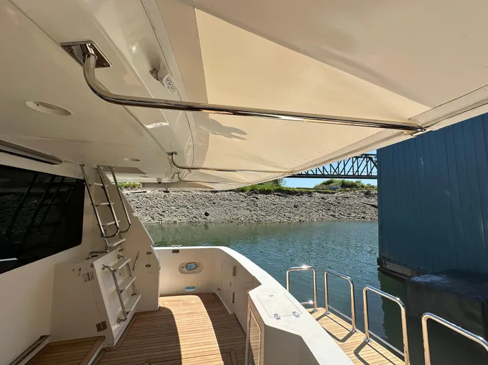 Safari Yacht Photos Pics 2001 Symbol 66 Pilothouse Yacht deck with awning, docked by a calm waterfront.