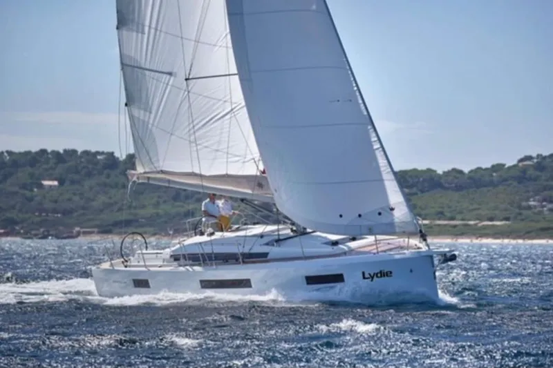  Yacht Photos Pics 2019 Jeanneau Sun Odyssey 440 sailing on open water, with lush coastline in the background.