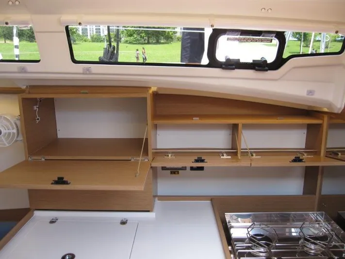  Yacht Photos Pics Interior of 2025 Jeanneau Sun Odyssey 350 yacht, featuring open wooden cabinets and a compact kitchen.