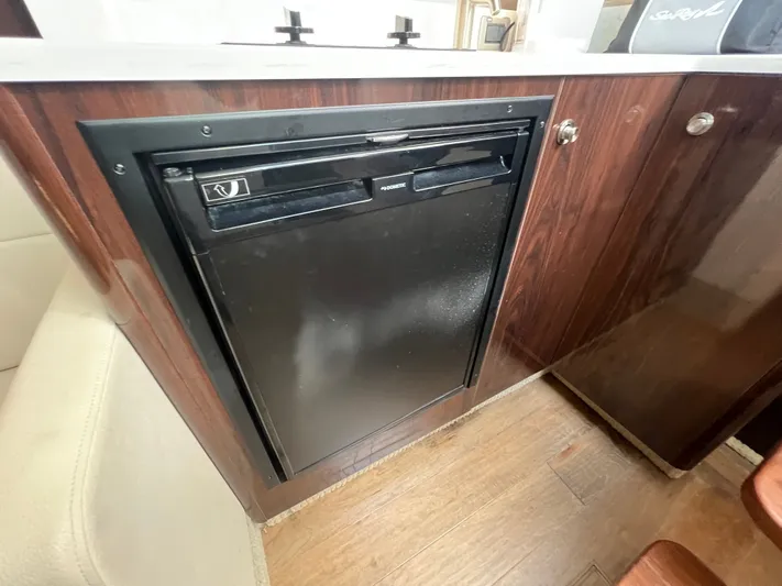  Yacht Photos Pics 2018 Sea Ray 350 Sundancer interior with compact black refrigerator and wooden cabinetry.