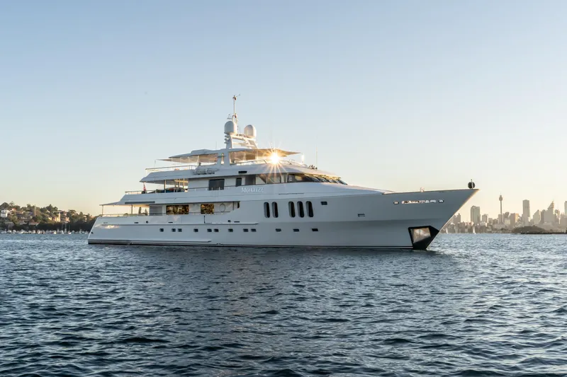 Moatize Yacht Photos Pics Luxurious 1998 Pendennis Custom yacht on serene water with city skyline backdrop.