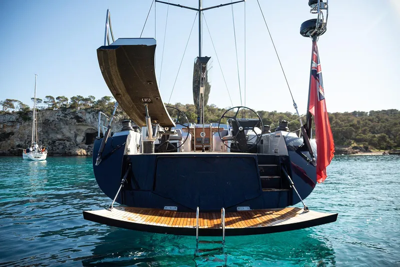 Caiarossa Yacht Photos Pics Stern view of 2009 Shipman 72 yacht with red flag, anchored in clear waters.