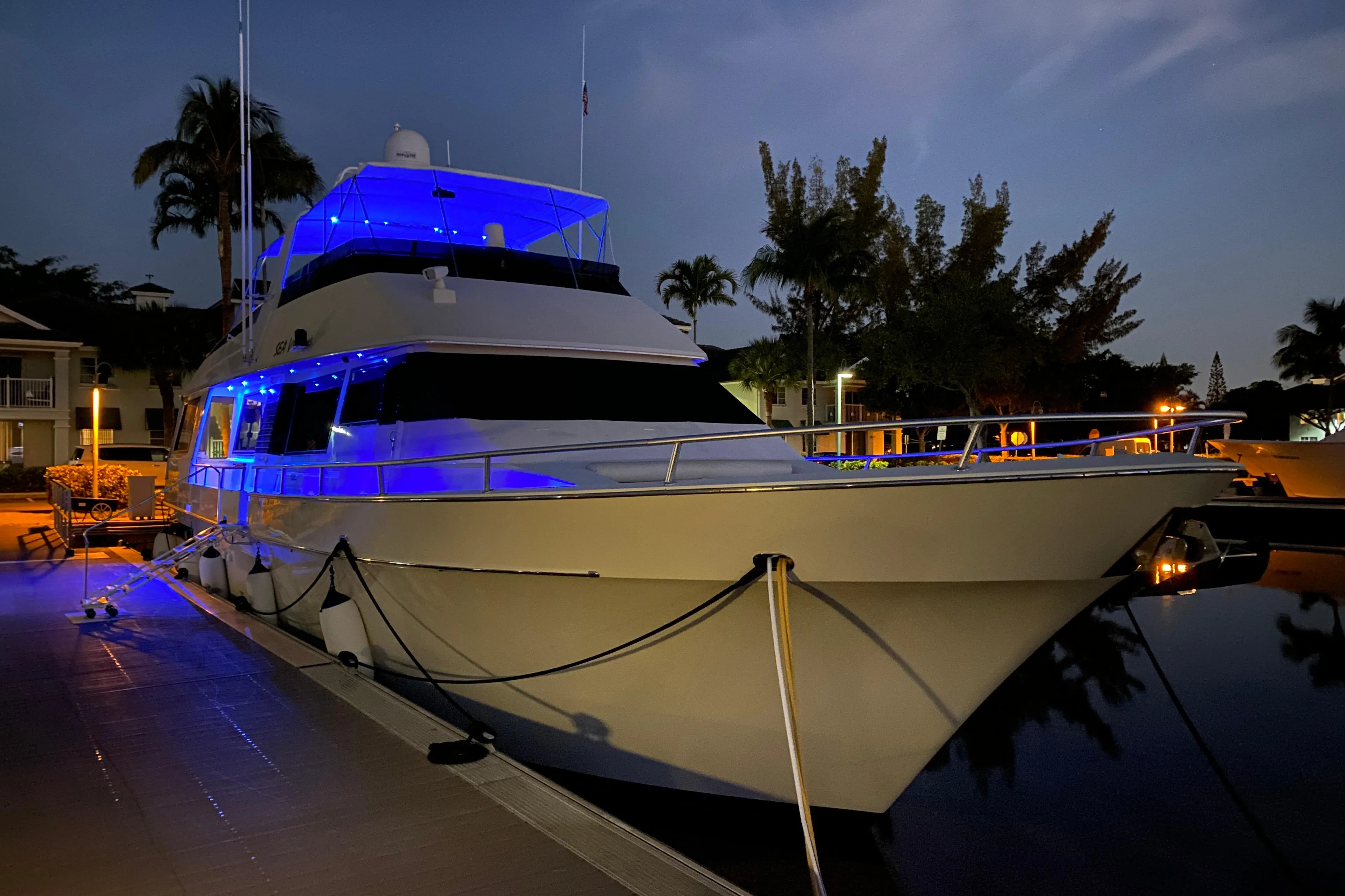 1991 Viking 65 Cockpit yacht illuminated with blue lights at night, docked near palm trees.