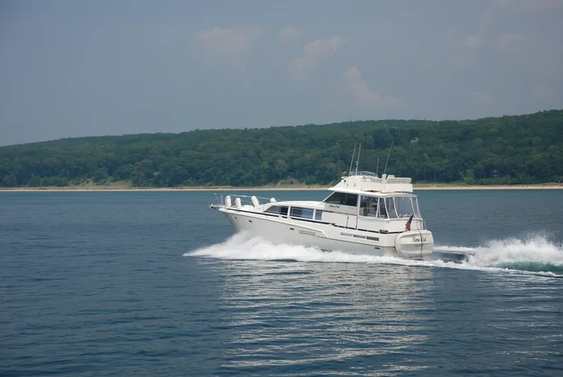  Yacht Photos Pics 1986 Bertram 46 Flybridge Motor Yacht cruising on a calm lake with forested shoreline.