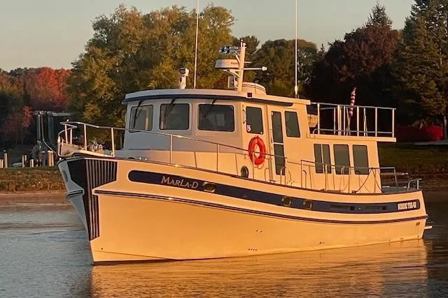  Yacht Photos Pics 2006 Nordic Tug 42 boat on calm water at sunset, surrounded by trees.