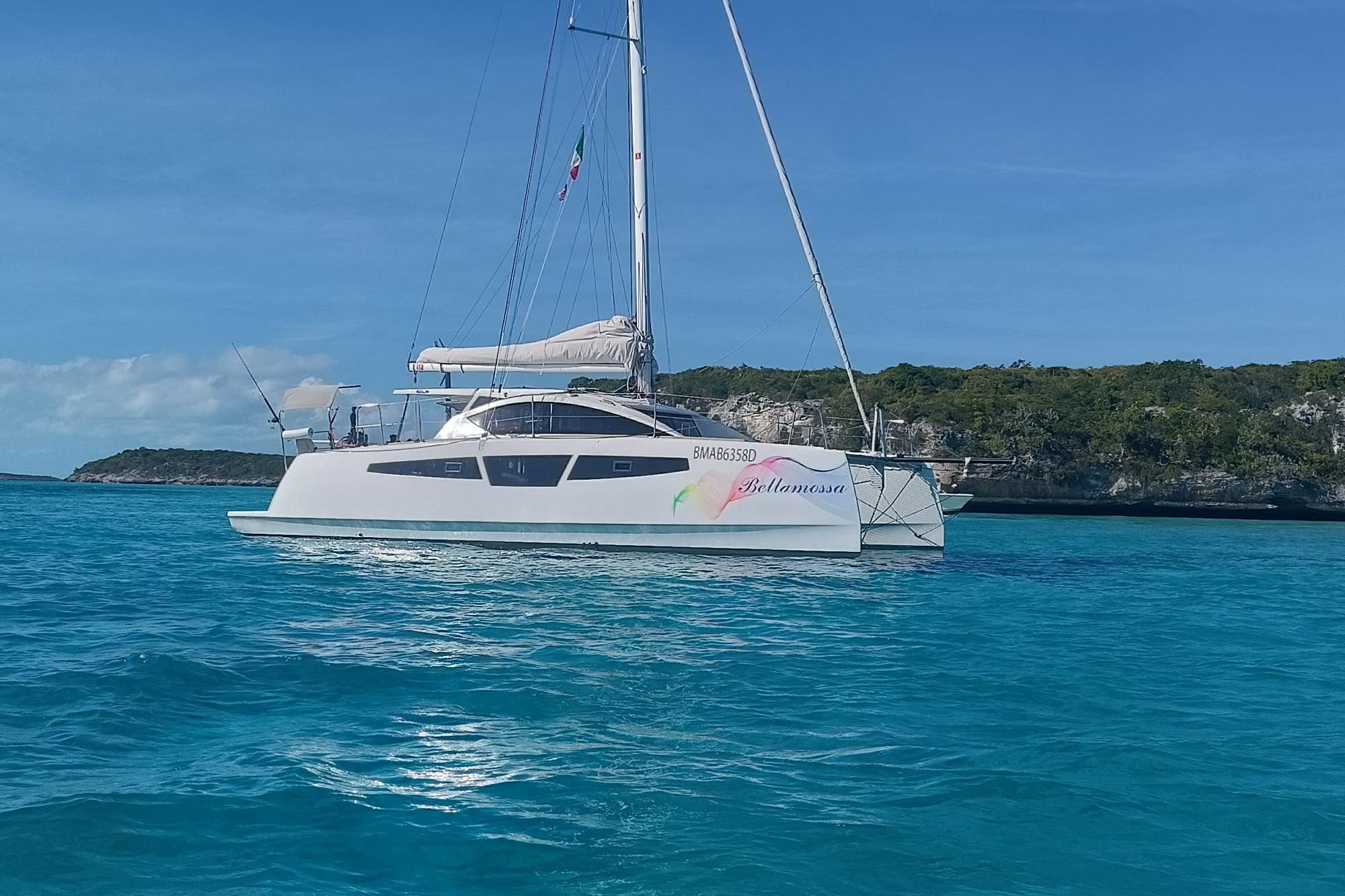 2026 C-Catamarans C-CAT 38 sailing in clear blue waters near a rocky coastline.
