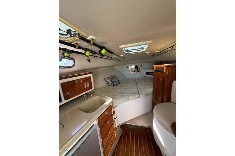  Yacht Photos Pics 2004 Pursuit 3370 Offshore cabin interior with bed, sink, and fishing rods.