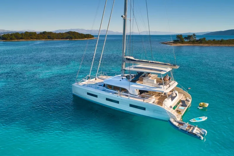 Amada Mia Yacht Photos Pics 2021 Lagoon Sixty5 catamaran sailing in clear turquoise waters near a small island.