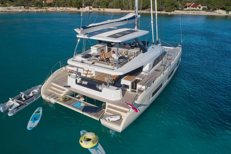 Amada Mia Yacht Photos Pics Luxury Lagoon Sixty5 yacht anchored in turquoise waters, featuring spacious deck and water sports equipment.