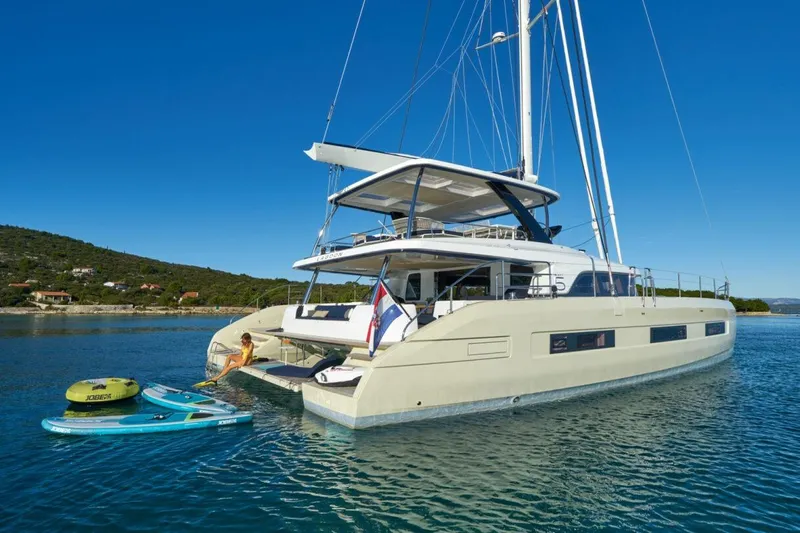 Amada Mia Yacht Photos Pics 2021 Lagoon Sixty5 yacht anchored with paddleboards and inflatable, under clear blue sky.