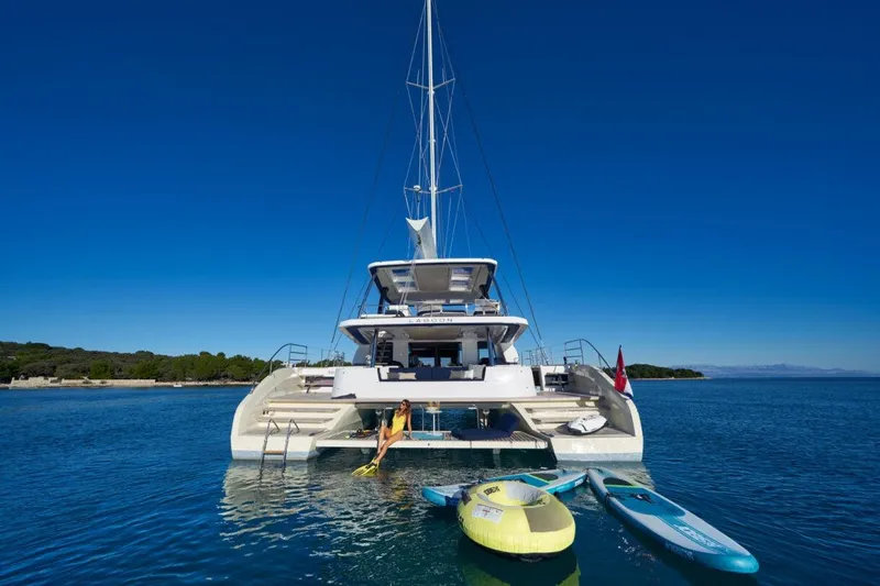 Amada Mia Yacht Photos Pics Luxurious 2021 Lagoon Sixty5 catamaran anchored with water sports equipment in serene blue waters.