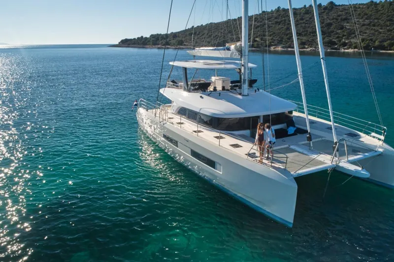 Amada Mia Yacht Photos Pics 2021 Lagoon Sixty5 catamaran sailing in clear blue waters near a scenic coastline.