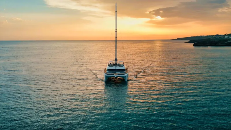 Feel The Blue Yacht Photos Pics Sunreef 60 catamaran sailing at sunset, 2018 model, on calm ocean waters.