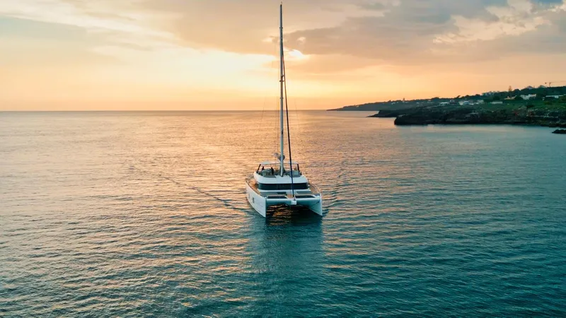 Feel The Blue Yacht Photos Pics Sunreef 60 catamaran sailing at sunset, 2018 model, on calm ocean waters.