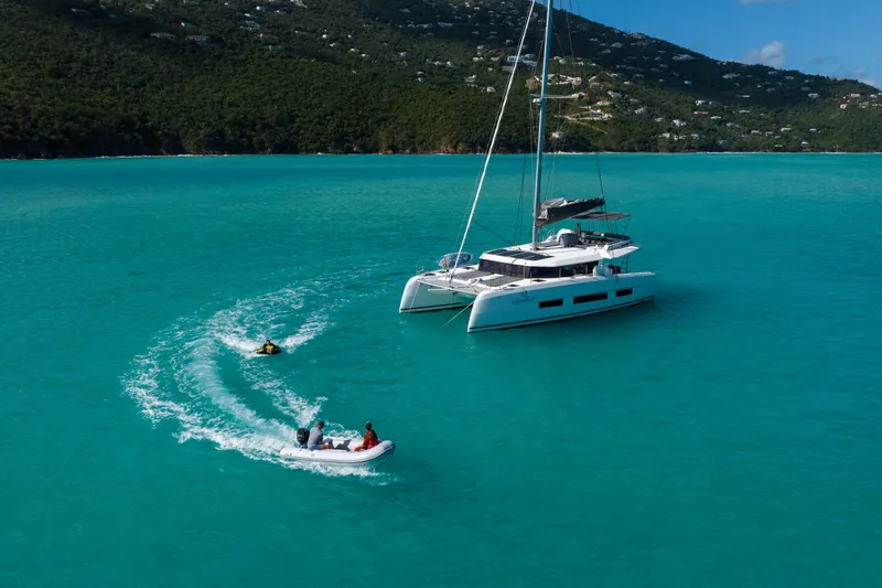 Aquanimity Yacht Photos Pics 2021 Dufour 48 catamaran anchored in turquoise waters with nearby dinghy and jet ski.