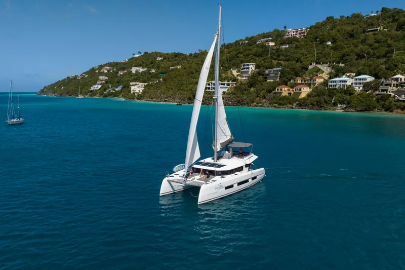 Aquanimity Yacht Photos Pics Sailing catamaran Dufour 48, 2021 model, cruising in turquoise waters near lush coastline.
