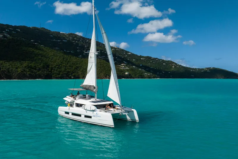 Aquanimity Yacht Photos Pics Sailing catamaran Dufour 48, 2021 model, cruising in turquoise waters near lush green hills.