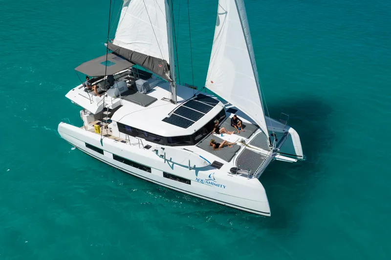 Aquanimity Yacht Photos Pics 2021 Dufour 48 catamaran sailing on turquoise waters with people relaxing on deck.