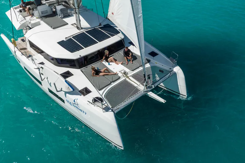 Aquanimity Yacht Photos Pics 2021 Dufour 48 catamaran sailing on turquoise waters with people relaxing on deck.