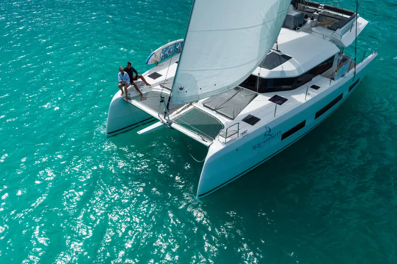 Aquanimity Yacht Photos Pics 2021 Dufour 48 catamaran sailing on clear turquoise waters, with two people relaxing on deck.