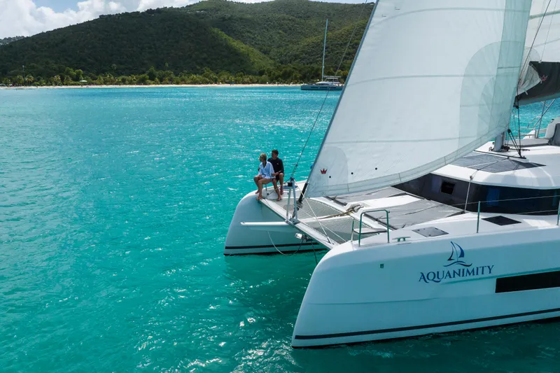 Aquanimity Yacht Photos Pics 2021 Dufour 48 catamaran sailing in turquoise waters near lush green hills.