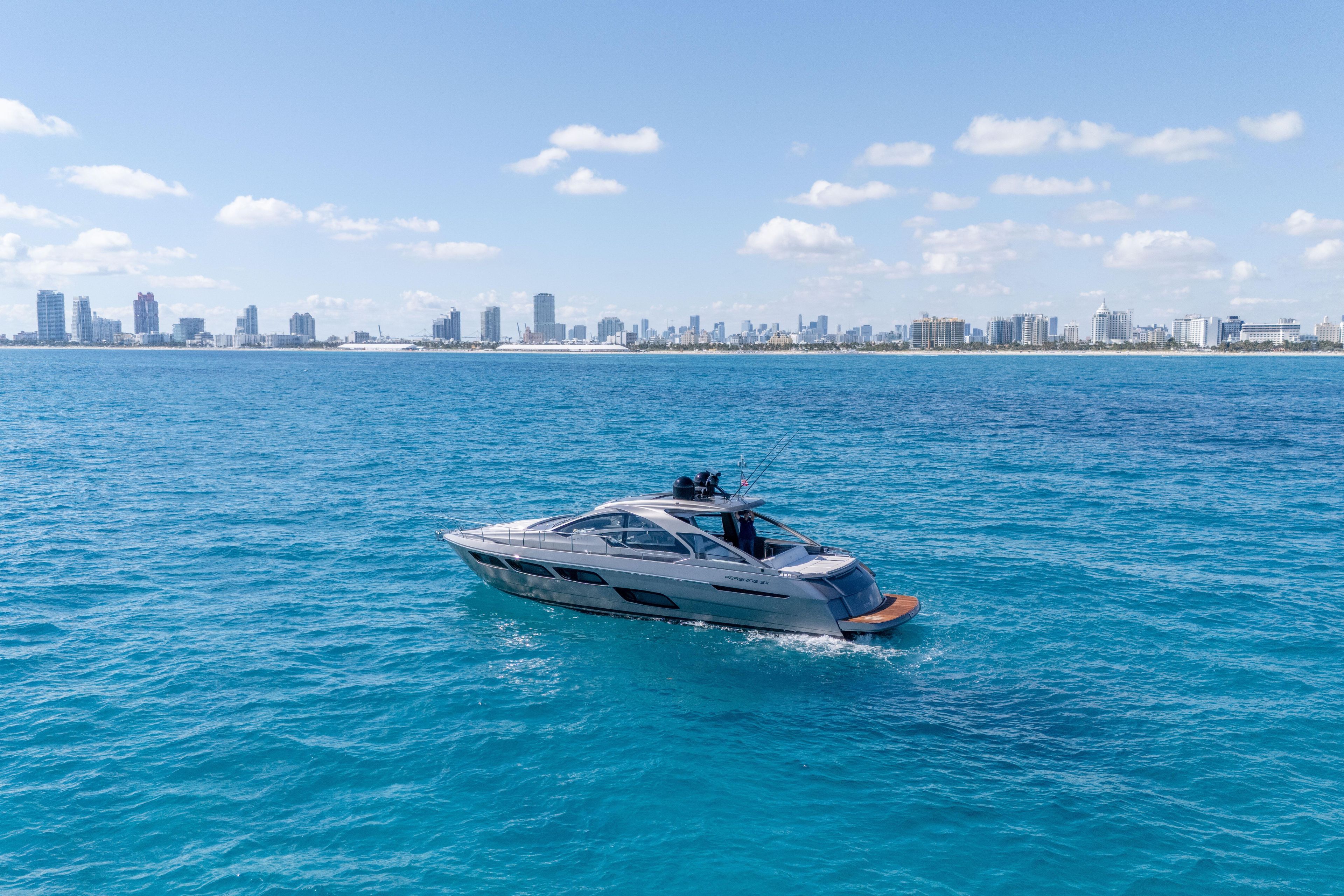 2019 Pershing 5x yacht cruising on blue ocean with city skyline in background.