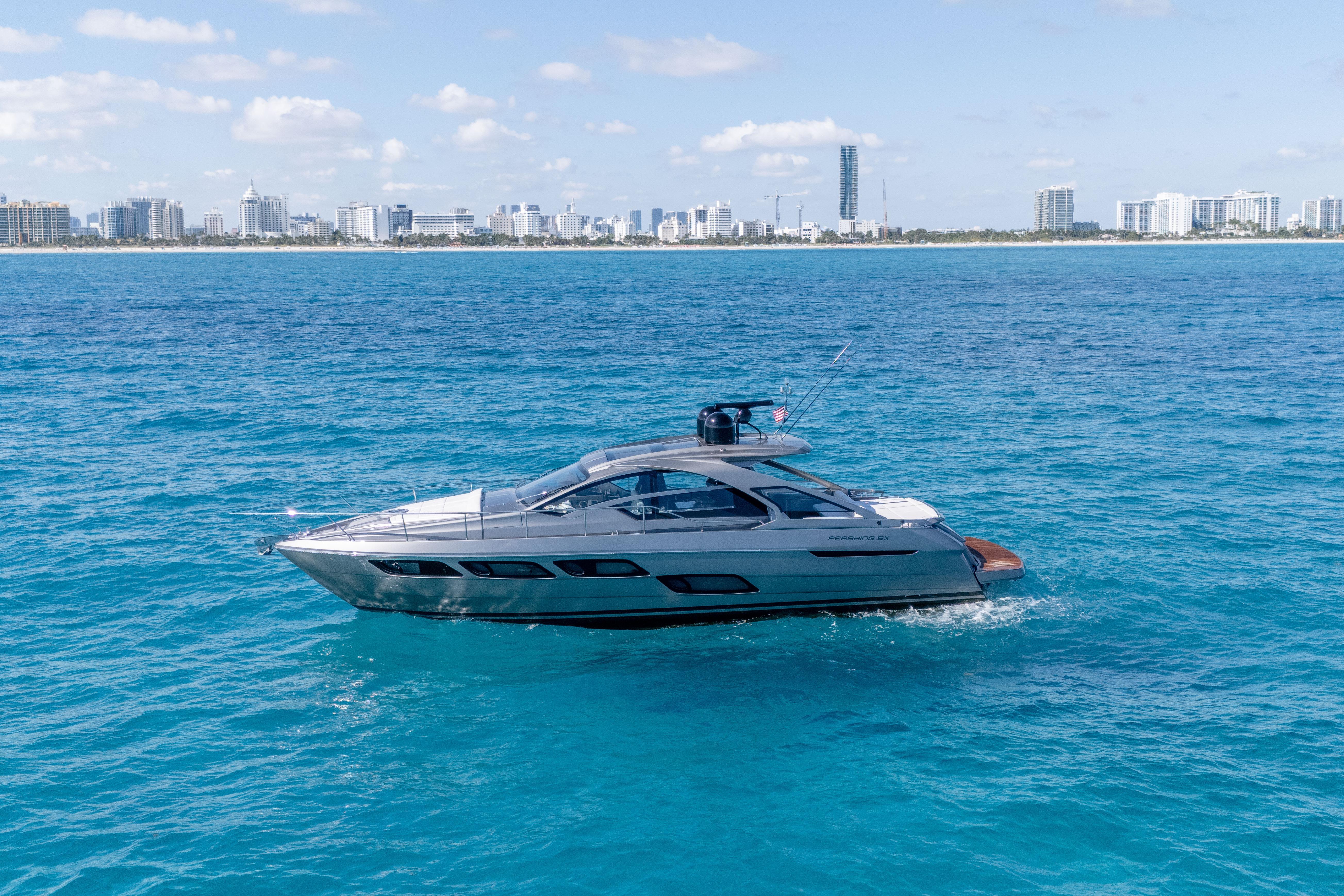 2019 Pershing 5x yacht cruising on blue ocean with city skyline in background.