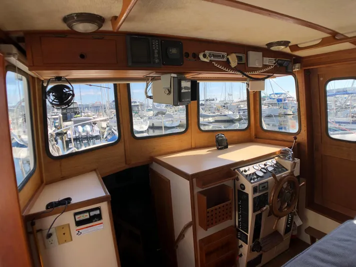  Yacht Photos Pics 1989 Nordic Tug 32 interior with wooden helm, navigation equipment, and marina view.