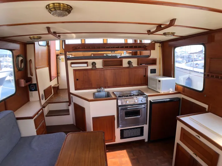  Yacht Photos Pics 1989 Nordic Tug 32 interior with kitchen, stove, sink, and microwave, showcasing wooden cabinetry.