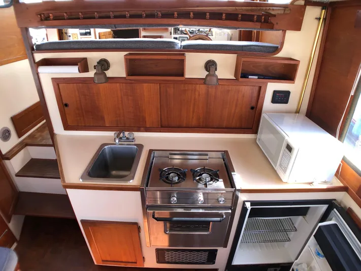  Yacht Photos Pics 1989 Nordic Tug 32 kitchen with stove, sink, microwave, and wooden cabinetry.