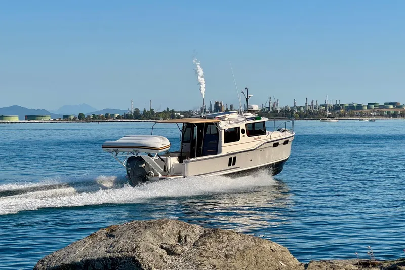 Noodles Yacht Photos Pics 2024 Ranger Tugs R-27 cruising on a sunny day near industrial shoreline.