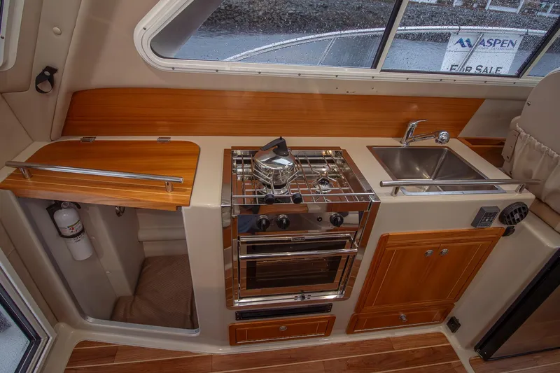  Yacht Photos Pics Compact kitchen in 2019 Aspen C107 boat with stove, sink, and wooden cabinetry.