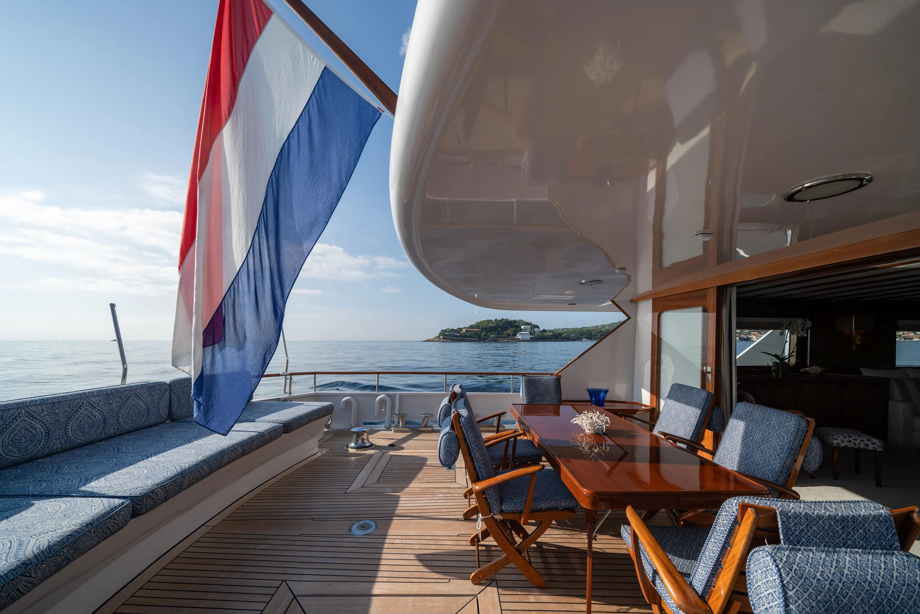 Bluemar II Yacht Photos Pics Feadship Classic 1978 yacht deck with Dutch flag, wooden table, and ocean view.
